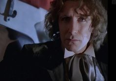 a man with curly hair wearing a suit and tie in front of a mirror looking at the camera