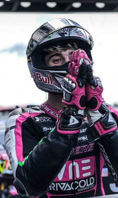 a man wearing a pink and black motorcycle suit holding his hand up to his face