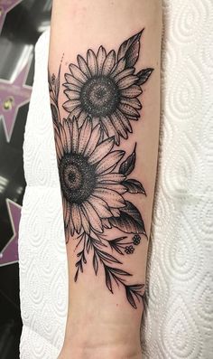 a sunflower tattoo on the arm with black and white flowers in front of it