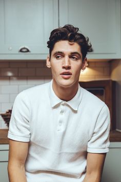 a young man in a white shirt and tie sitting on a kitchen counter looking at the camera