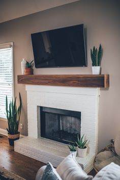 a flat screen tv mounted on the wall above a fireplace with potted cacti