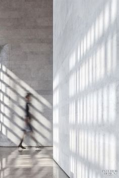 a woman is walking in an empty room with long shadows on the wall and floor