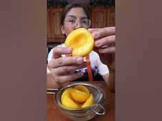 a woman holding a peeled mango in front of a glass bowl with the fruit inside