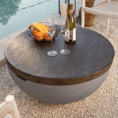 a table with two wine glasses and some fruit on it next to a swimming pool