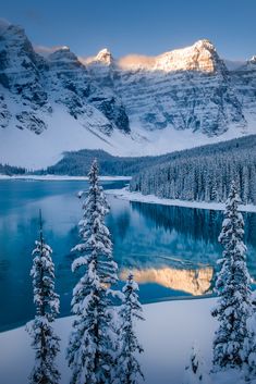 snow covered trees and mountains surrounding a lake