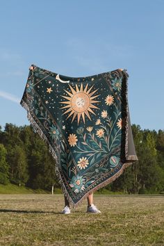 a person standing in the grass with a blanket over their head and sun design on it