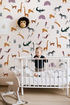 a baby sitting in a crib next to a wall with animals on it