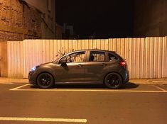 a small car parked in front of a white fence at night with its door open