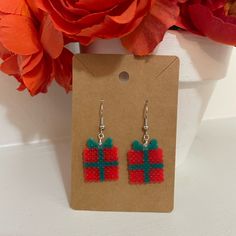 a pair of red and green earrings sitting on top of a card board next to a flower