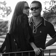 a man standing next to a woman on top of a wooden fence with a tree in the background