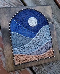 a piece of string art with mountains in the background and a full moon above it