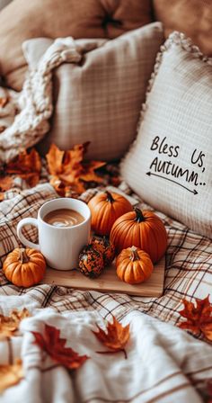 a cup of coffee and some pumpkins on a bed with the words, bliss us autumn