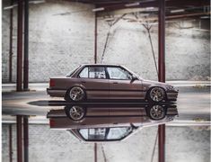 a car parked in front of a brick wall with its reflection on the water's surface