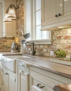 a kitchen with white cabinets and brick wall behind the countertop, along with an island