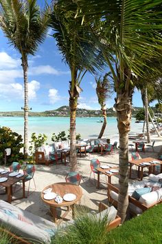 an outdoor dining area with tables and chairs on the beach next to palm trees in front of water