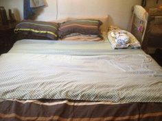 an unmade bed with several pillows and blankets on it in a small room next to a dresser