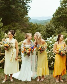 a group of women standing next to each other in front of trees and bushes holding bouquets