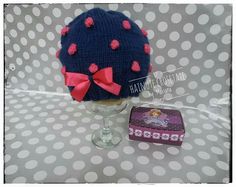 a knitted hat with pink bows sits on a table next to a small box