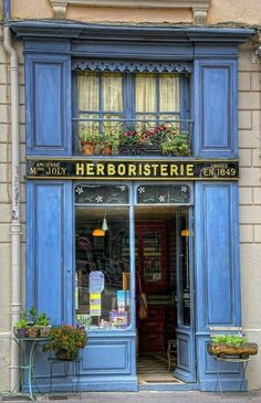 a store front with blue shutters and flowers on the window sill in front