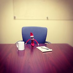 an elf doll sitting at a desk next to a cup