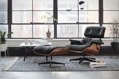 an eames chair and ottoman in front of large windows