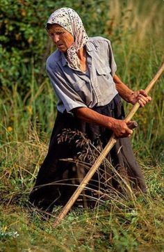 an old woman is standing in the grass with a stick