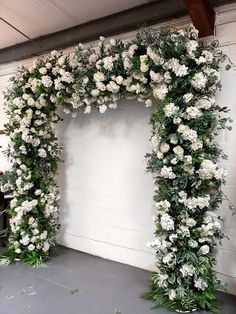 white flowers and greenery are arranged in an arch