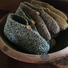 three knitted slippers in a metal bowl on a wooden table, with buttons