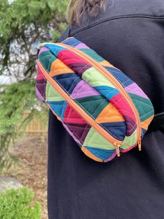 a woman wearing a black shirt and colorful patchwork fanny bag on her back with trees in the background