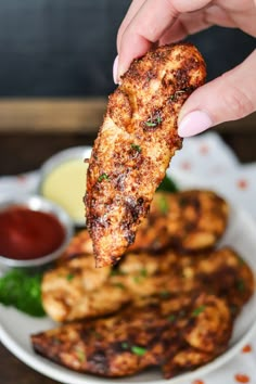 a person is holding up a piece of chicken on a plate with other food items