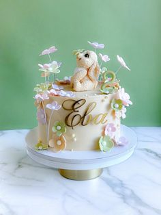 there is a cake with flowers and a teddy bear sitting on the top one tier