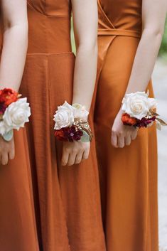 three bridesmaids in orange dresses hold their bouquets with white and red flowers