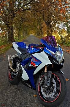 a blue and white motorcycle parked on the side of a road in front of trees