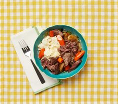 a bowl filled with meat and vegetables on top of a yellow checkered table cloth