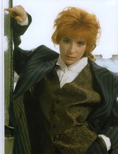 a woman with red hair is leaning against a pole and posing for the camera while wearing a suit