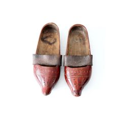 This is a pair of antique wooden clogs. The hand-carved wood sabot feature a red lacquer paint with leather straps across the arch. Vintage Clogs With Leather Sole And Closed Toe, Vintage Leather Sole Closed Toe Clogs, Vintage Closed Toe Clogs With Leather Sole, Vintage Closed Toe Mules With Leather Sole, Vintage Leather Sole Slip-on Clogs, Traditional Brown Slip-on Clogs, Traditional Slip-on Clogs With Rubber Sole, Traditional Leather Clogs With Closed Toe, Traditional Leather Closed-toe Clogs