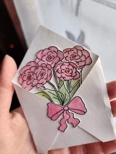 a hand holding an envelope with flowers in it and a pink bow on the front