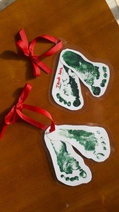 two hand and foot prints are hanging from a red ribbon on a wooden table top