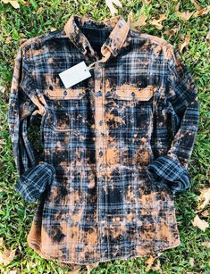 a black and brown flannel shirt laying on top of green grass with a tag