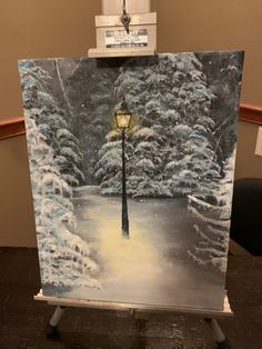 an easel with a painting of a street light in the snow and trees behind it