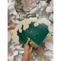 a person holding up some cards in front of white paper flowers and leaves on the wall