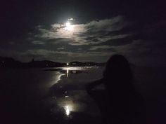 a woman standing on the beach at night with her back turned to the camera and full moon in the background