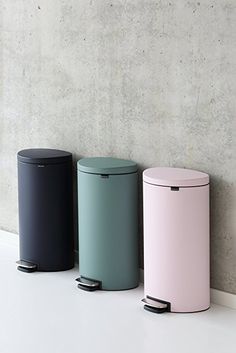 three trash cans are lined up against a wall, one is pink and the other is blue