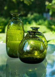 two green vases sitting on top of a table next to each other in front of trees