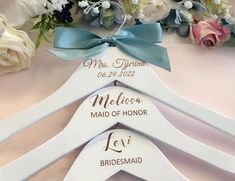 three personalized wedding hangers with bows and flowers in the background on a table