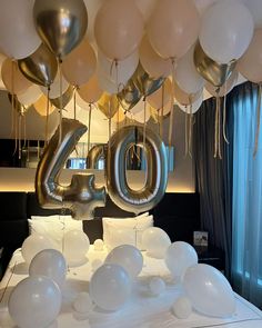 balloons are floating in the air above a bed that is decorated with white and gold balloons