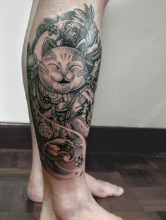 a cat tattoo on the leg of a person's legs with flowers and leaves