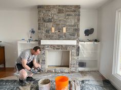 a man working on a fireplace in a living room with paint buckets next to it