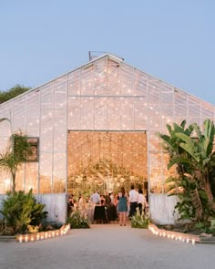 people are standing in front of a large glass building with lights on the outside and inside