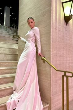 a woman in a long pink dress leaning against a wall with her hand on the railing